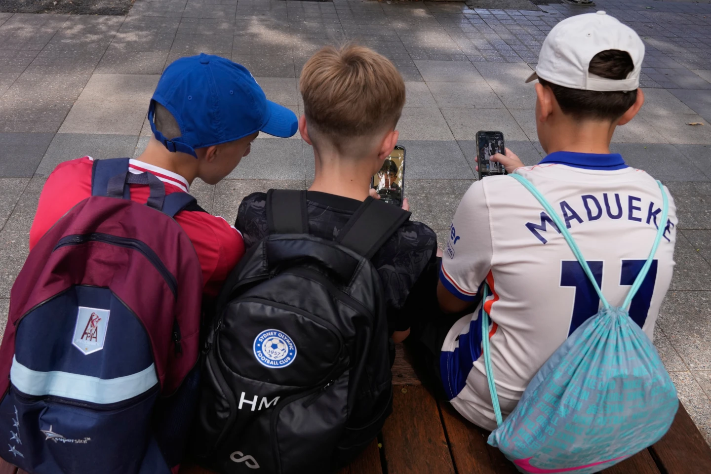 Hugo Winwood-Smith, right, Hardy Macpherson and Edan Abou, left, all 11-years-old, use their phones while sitting outside a school in Sydney, Monday, Dec. 8, 2025