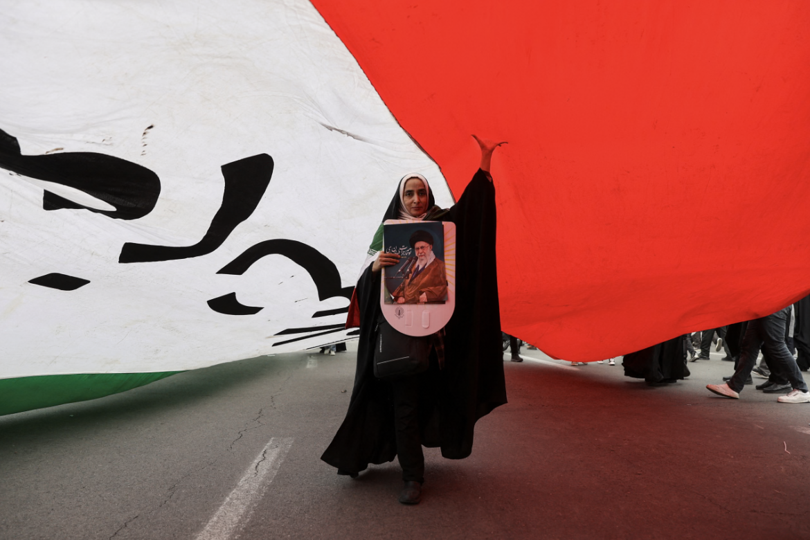 An Iranian woman holding a poster depicting Iran’s Supreme Leader Ayatollah Ali Khamenei walks under a large flag during the forty-seventh anniversary of the Islamic Revolution in Tehran, Iran, on February 11, 2026.