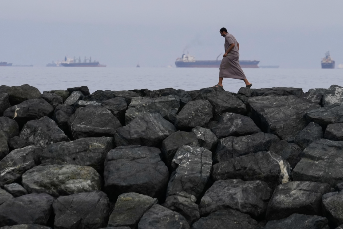 A man walks along the shore as oil tankers and cargo ships line up in the Strait of Hormuz, seen from Khor Fakkan, United Arab Emirates, Wednesday, March 11, 2026.