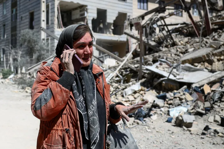 A woman talks on a phone amid a damaged residential neighbourhood, as the US-Israel war on Iran continues, in Tehran, March 30, 2026