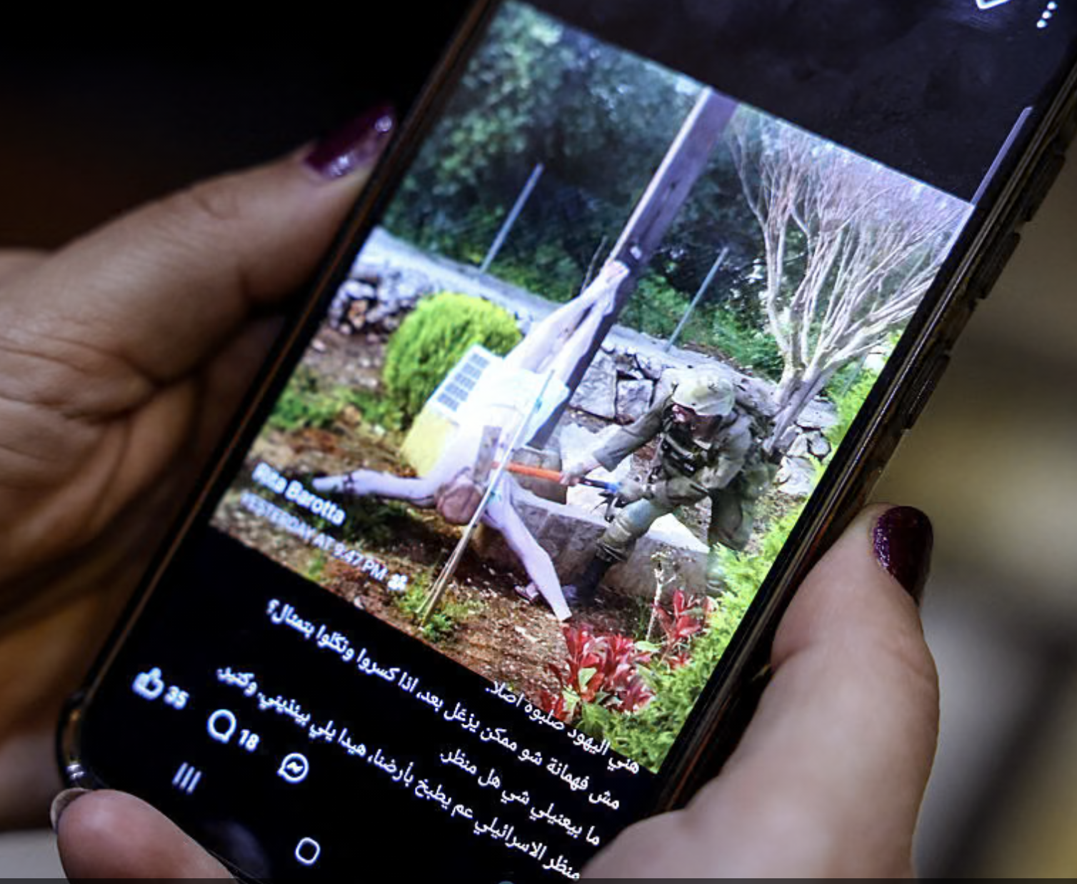 A woman checks a social media post on her mobile phone featuring an image that appears to show an Israeli soldier hitting a statue of Jesus Christ in the southern Lebanese Christian village of Debel, in Beirut on April 20, 2026. The photo, which the military determined was authentic after it spread online, shows an Israeli soldier using a sledgehammer to strike the head of a statue of a crucified Jesus.