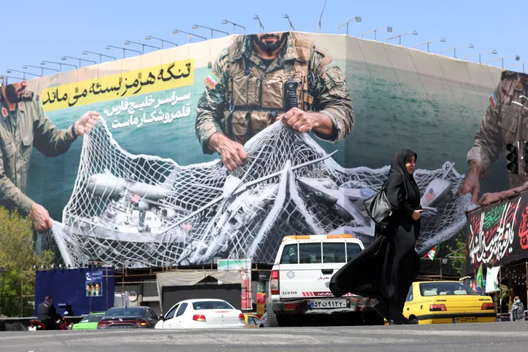 Traffic passes a billboard reading, ’The Strait of Hormuz will remain closed,' in Enghelb Square in Tehran