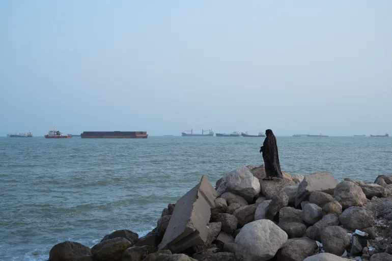 A women stands overlooking the water as ships are seen anchored in the Strait of Hormuz on August 10, 2026, off the coast of Bandar Abbas, Iran